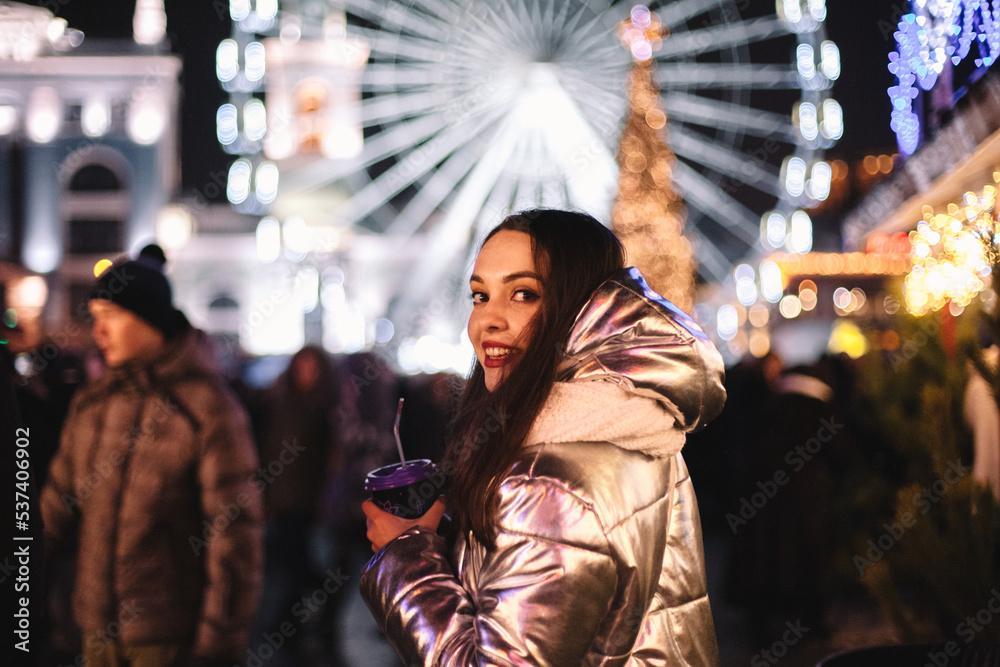 Happy young woman looking back while walking in Christmas market in city at night