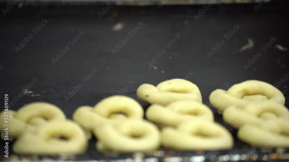 Cookies production line (sweet and salty cookies) in a factory. A chef smears unbaked cookies with egg yolk and garnish with sesame seeds and nigella sativa. 4K Video Food factory production concept. Cookies production line (sweet and salty cookies) in a factory. A chef smears unbaked cookies with egg yolk and garnish with sesame seeds and nigella sativa. 4K Video Food factory production concept.