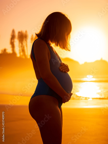 Pregnant woman on ocean beach at sunrise or sunset