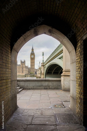 Fotografia, Obraz View of Big Ben, Palace of Wesminster and Westminster Bridge with cloudy sky background through an archway under the bridge