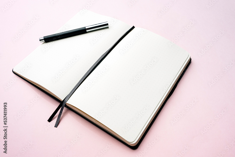 Open bullet journal with a pen on pastel pink background. Open notebook ready to be written on. Open bullet journal with a pen on pastel pink background. Open notebook ready to be written on.
