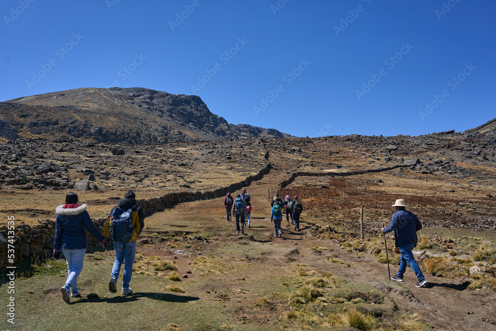 Grupo de turistas escalando y subiendo a pie una montaña con vegetación en los andes peruanos 