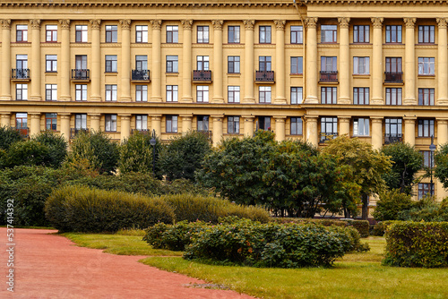 Facade of a yellow building with windows and balconies, next to a park. European house with columns. © Alex Chebak