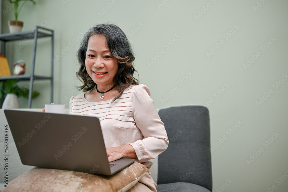 Joyful 60s retired-asian woman using laptop computer in the living room. Joyful 60s retired-asian woman using laptop computer in the living room.