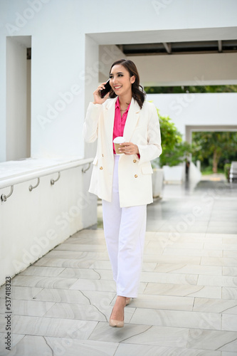 Successful Asian businesswoman on the phone while walking along of the company building.