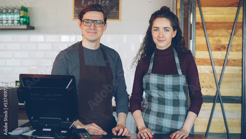 Portrait of two partners small business owners standing at cashier's desk in new coffee-house and smiling. Successful business, happy people and food service concept.