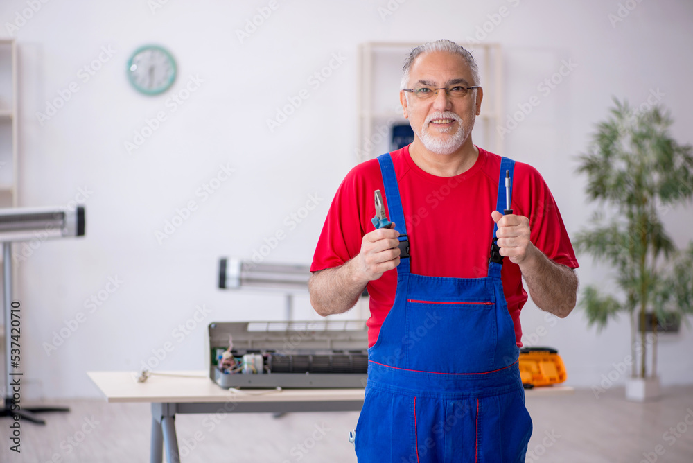 Old repairman repairing air-conditioner at workshop
