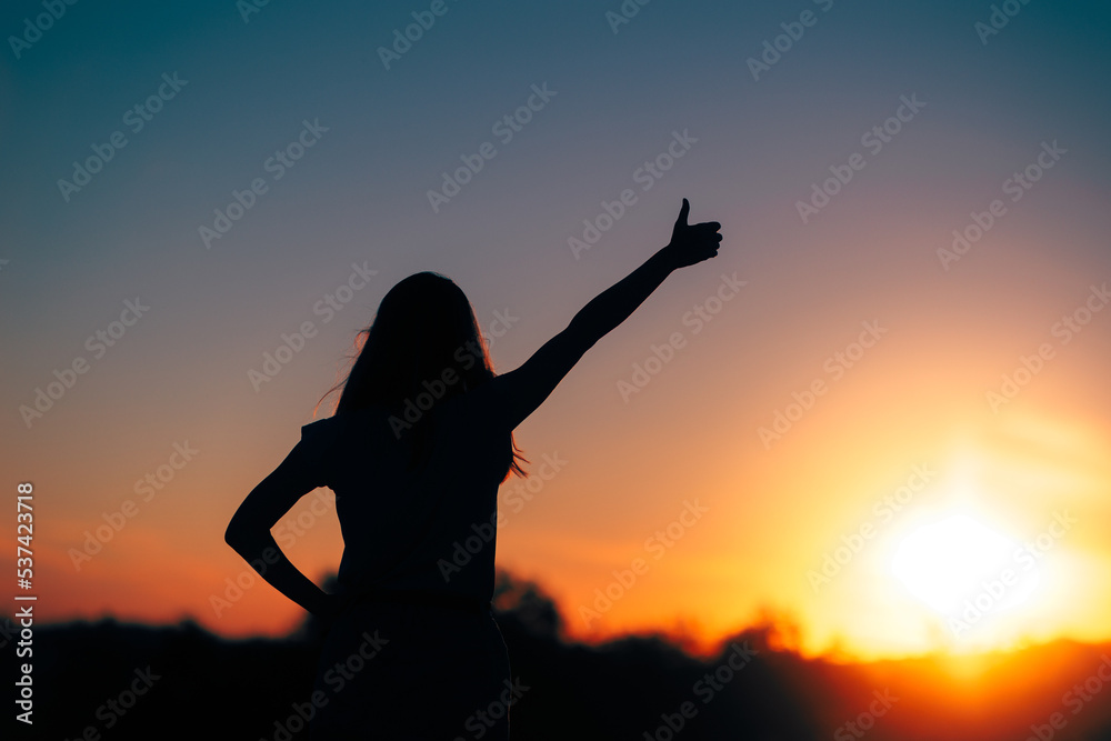 Back View Backlit silhouette of a Woman Holding Thumbs Up. Cheerful celebrating winner feeling lucky and successful

