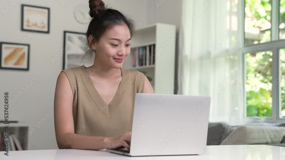 Young Asian woman using laptop at home, looking at screen, chatting, reading or writing email, sitting on desk, serious female student doing homework, working on research project online. Young Asian woman using laptop at home, looking at screen, chatting, reading or writing email, sitting on desk, serious female student doing homework, working on research project online.
