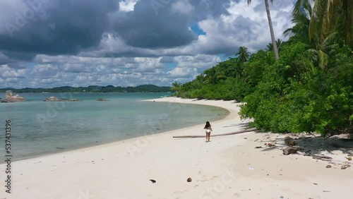 aerial of young asian girl running on empty white sand beach on tropical island in belitung indonesia photo