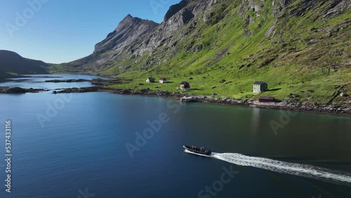 Motorboat passing traditional Rorbuer houses on the coast of sunny Kjerkfjorden, Lofoten, Norway - Aerial view photo