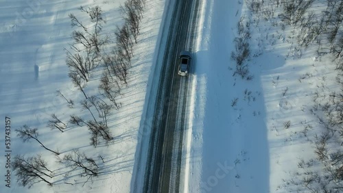 Aerial view tracking a car driving on a slippery, winter road in Lapland - high angle, drone shot photo