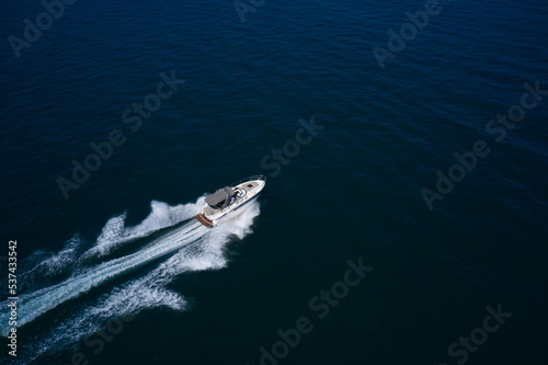 a high-speed big boat with people moves quickly on dark blue water making a white trail behind the boat. © Berg