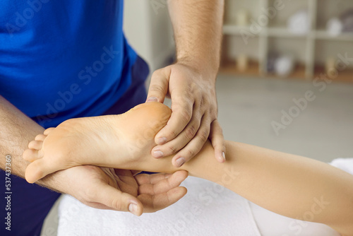 Crop close up of male masseur work with patient feet relieve strain muscles. Man physiotherapist massage client leg help with cramps or spasm. Saloon procedure. Physiotherapy and rehabilitation.