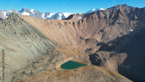 The emerald color of the water of a mountain lake. Drone view of a green mountain lake with a reflection of the mountains. Smooth transparent water. There are large stones nearby. Dry grass Kazakhstan photo