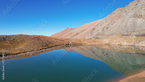 The emerald color of the water of a mountain lake. Drone view of a green mountain lake with a reflection of the mountains. Smooth transparent water. There are large stones nearby. Dry grass Kazakhstan photo