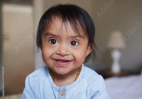 Happy, portrait smile and Down syndrome baby relaxing on a bed in happiness at home. Cheerful little child with genetic disorder or disability smiling in bedroom for cute childhood and development photo