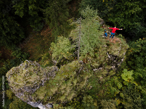 Hiker, middle-aged climber is on rock, surrounded by forest and makes recording of himself with a drone, lilienfeld, austria photo