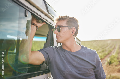 Travel, adventure and man by his car in the countryside while on a roadtrip during summer vacation. Sunshine, outdoors and young person in nature, relax on journey and traveling lifestyle. © S Fanti/peopleimages.com