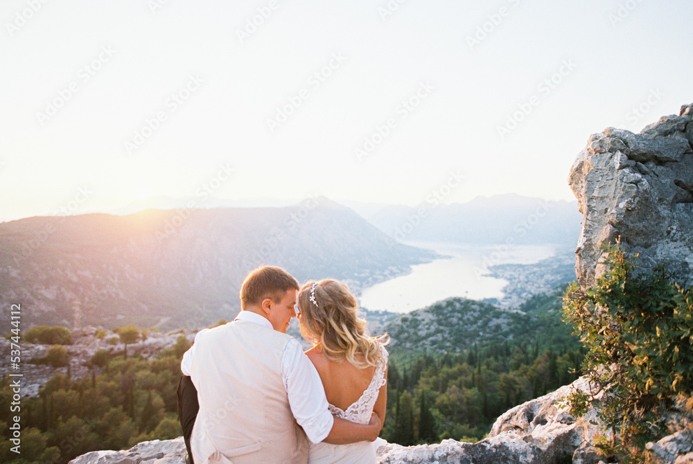 Bride and groom sit hugging on a mountain overlooking the Kotor Bay. Montenegro