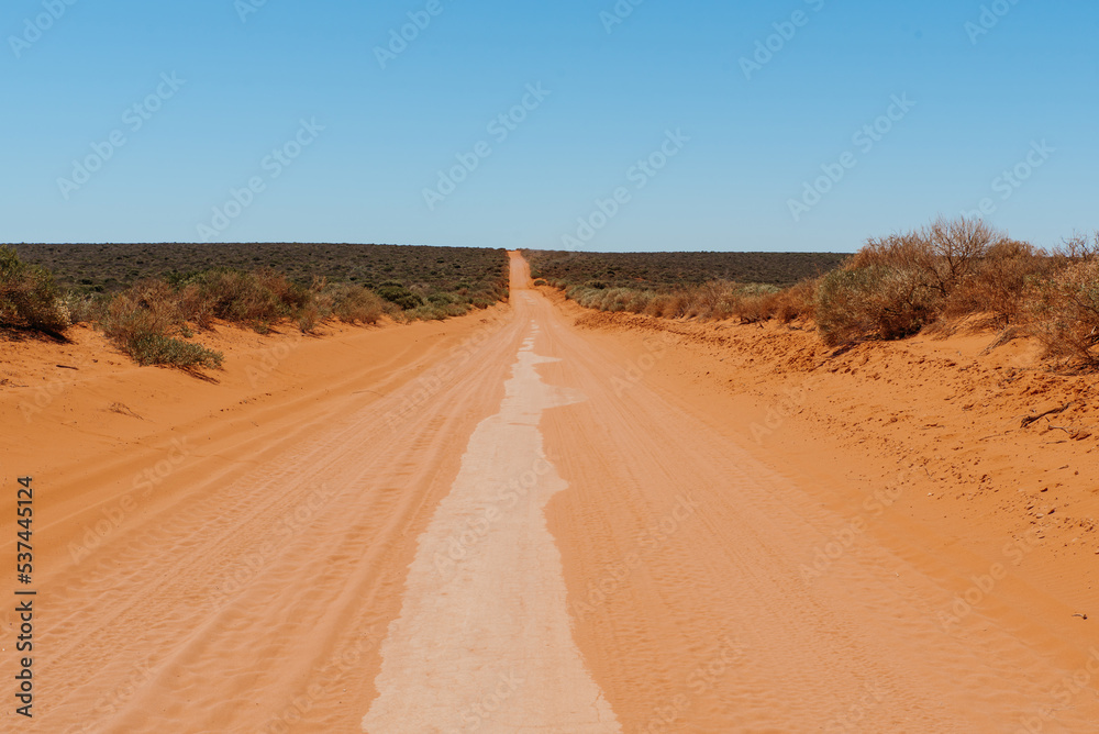 Australian outback red dirt road. Remote track in Australian bushland against clear blue sky Australian outback red dirt road. Remote track in Australian bushland against clear blue sky