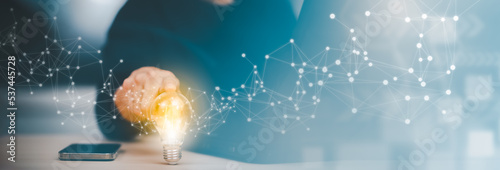 Quadro su tela Businessman hand holding light bulb with icons and working on the desk, Creativity and innovation are keys to success