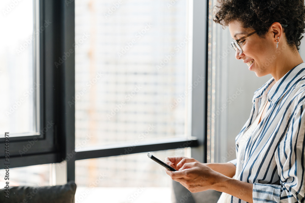 Young black woman in eyeglasses smiling and using mobile phone