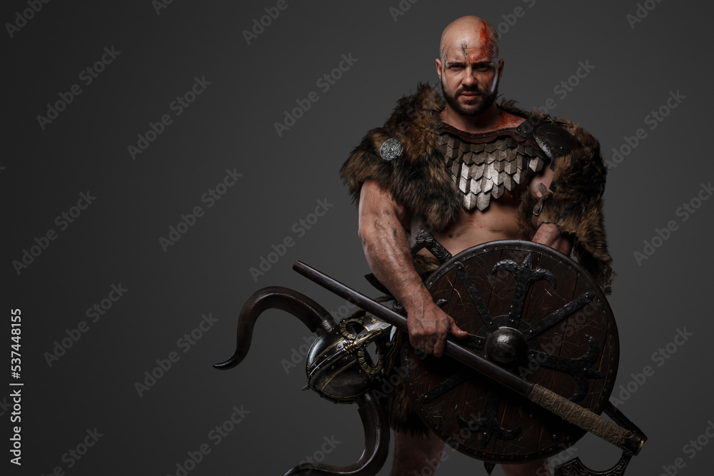 Portrait of nordic warrior with muscular build and horned helmet against gray background. Portrait of nordic warrior with muscular build and horned helmet against gray background.