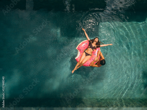 Young couple relaxing on an inflatable ring in a resort swimming pool. Happy young couple having fun on their honeymoon vacation photo