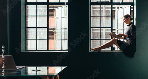 Woman reading a magazine while sitting at the window sill in her office