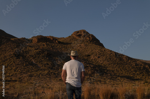 Rear view of adult man in cowboy hat in desert against mountain and sky. Almeria, Spain © WeeKwong