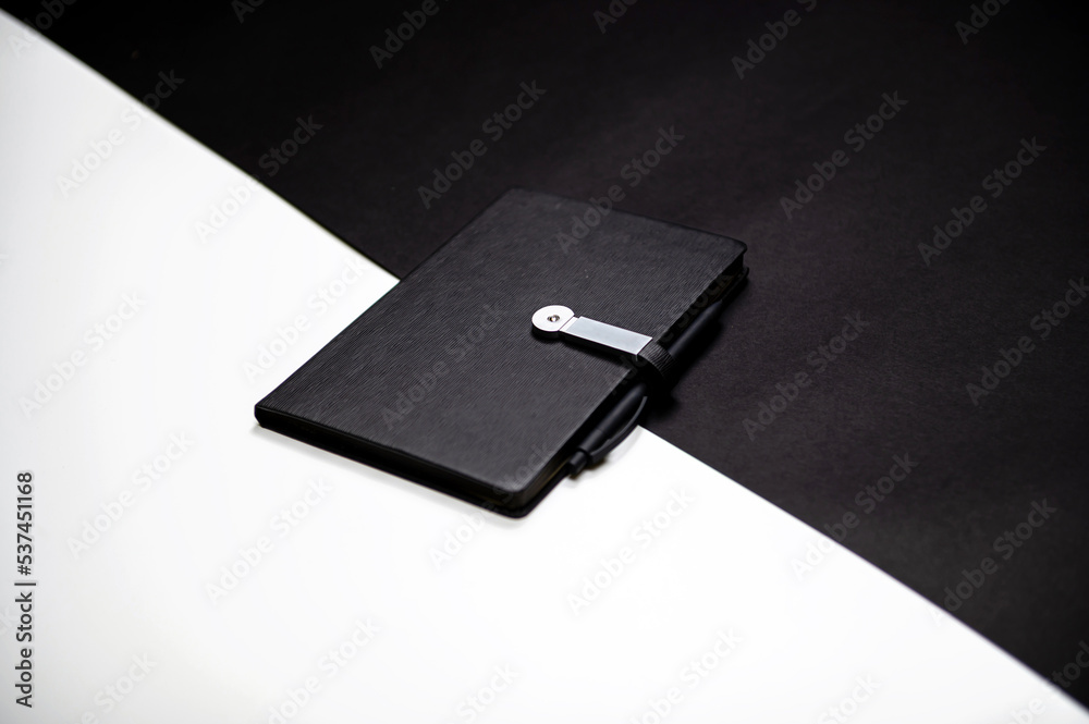 black organizer or notebook with pen on two-color black and white background, mockup, copy space black organizer or notebook with pen on two-color black and white background, mockup, copy space