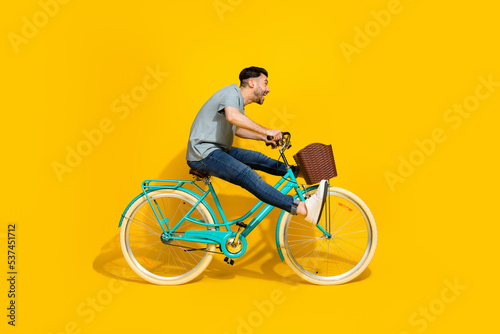 Side profile photo of young active energetic man driving new retro bicycle legs up crazy hurry fast speed look empty space isolated on yellow color background