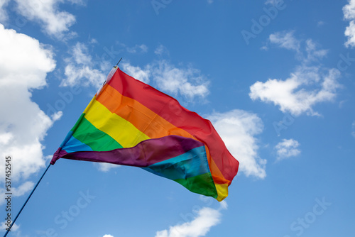 Regenbogenflagge vor blauem Himmel mit Wolken bei einer Parade zum CSD	
