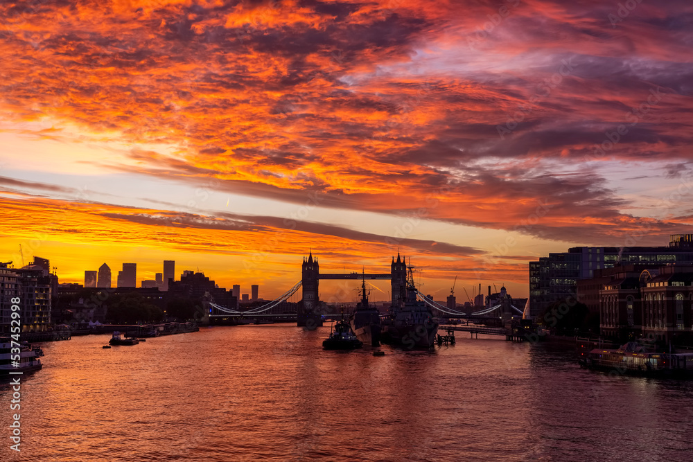A intense, red sunrise behind the skyline of London, England, with the famous Tower Bridge and River Thames