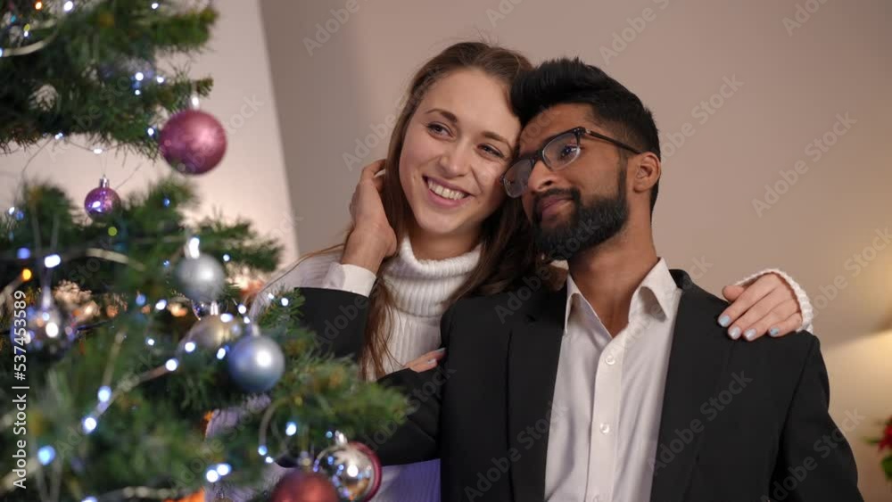 Loving girlfriend hugging happy boyfriend decorating Christmas tree on holiday. Portrait of beautiful Caucasian woman and handsome Middle Eastern man celebrating New Year's eve together Loving girlfriend hugging happy boyfriend decorating Christmas tree on holiday. Portrait of beautiful Caucasian woman and handsome Middle Eastern man celebrating New Year's eve together
