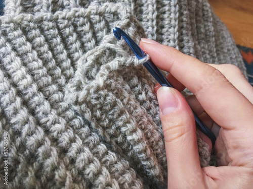 
Crochet hook with gray woolen winter scarf collar, crocheting antistress therapy. English rib stitch with a single crochet, hygge concept photo