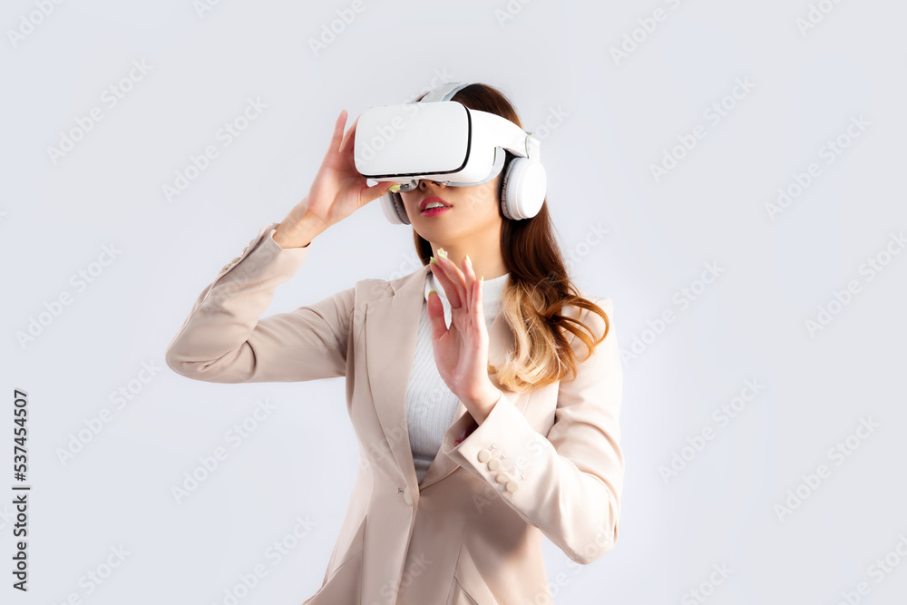 Asian businesswoman in beige color jacket suit wearing vr goggles hand touching on white screen background. Asian businesswoman in beige color jacket suit wearing vr goggles hand touching on white screen background.