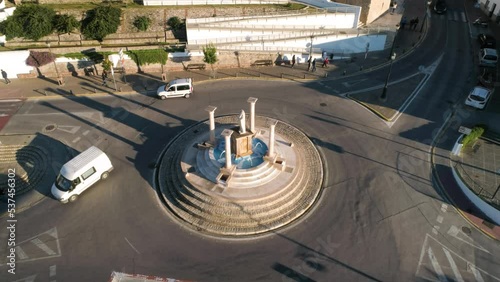 Aerial rotating shot of a traffic circle in medina sidonia in spain andalucia with a monument with fountain, columns and stone steps during car traffic on a sunny evening. Cádiz photo
