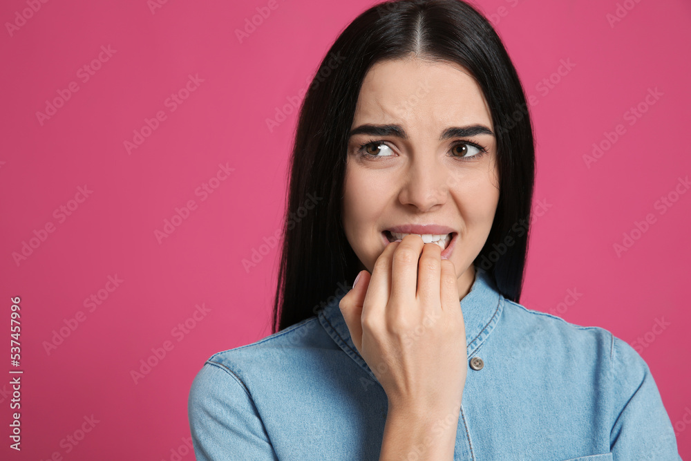 Young woman biting her nails on pink background Young woman biting her nails on pink background