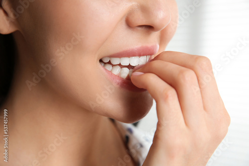 Young woman biting her nails on blurred background, closeup