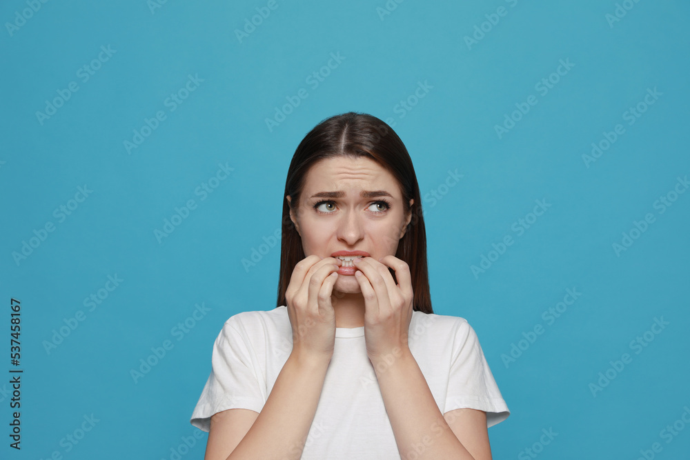 Young woman biting her nails on light blue background Young woman biting her nails on light blue background