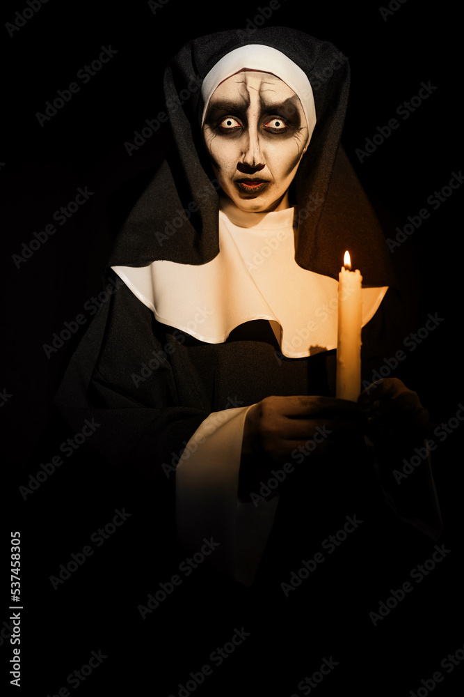 Scary devilish nun with burning candle on black background. Halloween party look Scary devilish nun with burning candle on black background. Halloween party look
