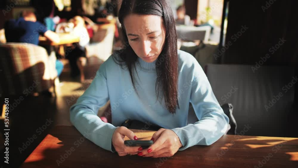 Portrait young beautiful businesswoman sitting in cafe or restaurant, holds in hands and using mobile phone for typing message or reading news. Remote work or online communication in cozy coffee shop. Portrait young beautiful businesswoman sitting in cafe or restaurant, holds in hands and using mobile phone for typing message or reading news. Remote work or online communication in cozy coffee shop.