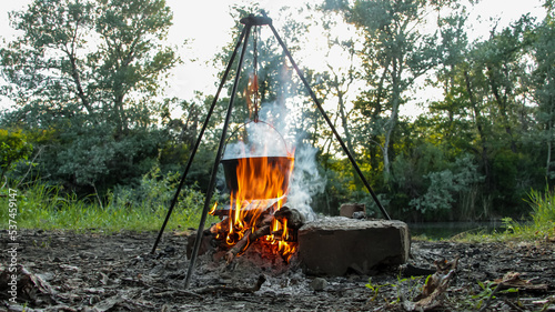 Fototapeta Naklejka Na Ścianę i Meble -  Relaxing and cooking over a campfire in the woods on a fishing trip. Summer mood, outdoor food in the forest. Cooking shish kebab and fish soup on a campfire at a picnic outside the city.