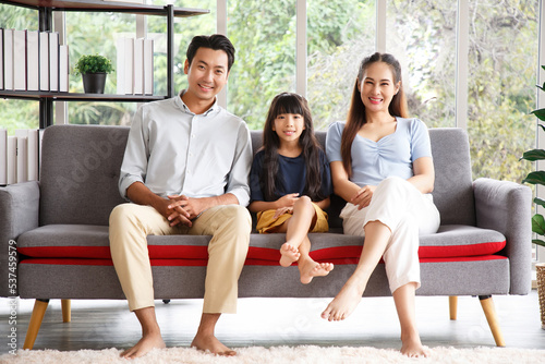 Portrait of a happy young family. Mom, dad and daughter look at the camera and smile. The faces of Asian parents and their child in living room.
