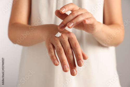 Woman applying cosmetic cream onto hand against light grey background  closeup