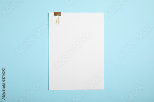 Sheet of paper with clip on light blue background, top view