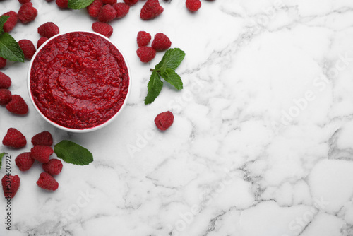 Raspberry puree in bowl and fresh berries with mint on white marble table, flat lay. Space for text