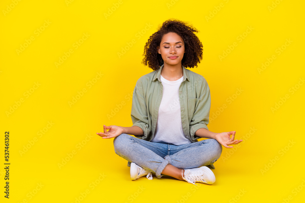 Full length photo of cute young lady curly hair sit lotus pose enjoy meditate wear trendy khaki clothes isolated on yellow color background Full length photo of cute young lady curly hair sit lotus pose enjoy meditate wear trendy khaki clothes isolated on yellow color background